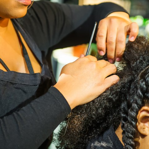 Professional stylist braiding textured hair with precision tools during salon service