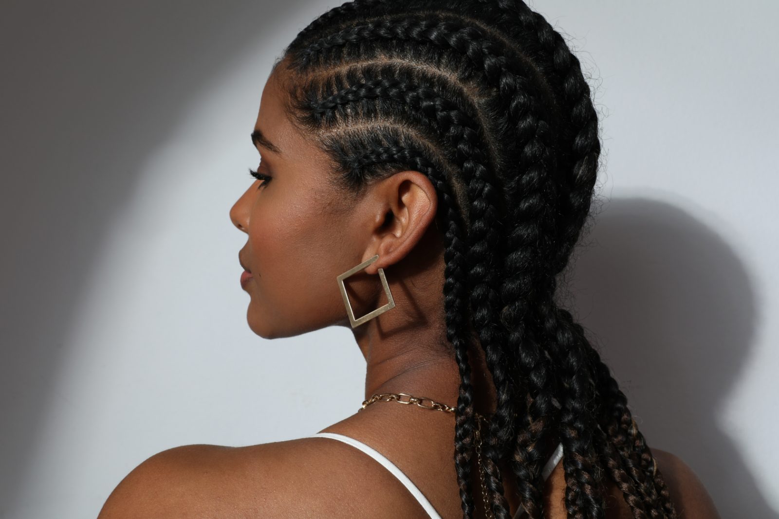 Woman with braided hairstyle wearing square earrings and chain necklace, side profile view