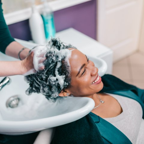 Hairdresser washing client's hair at salon sink with shampoo